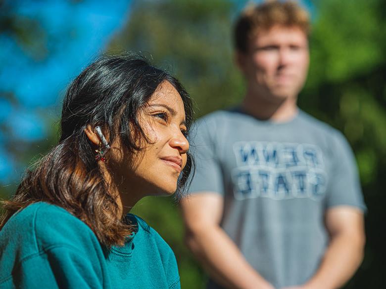 A female student sits near the campus Railroad clock while a male students stands in the background